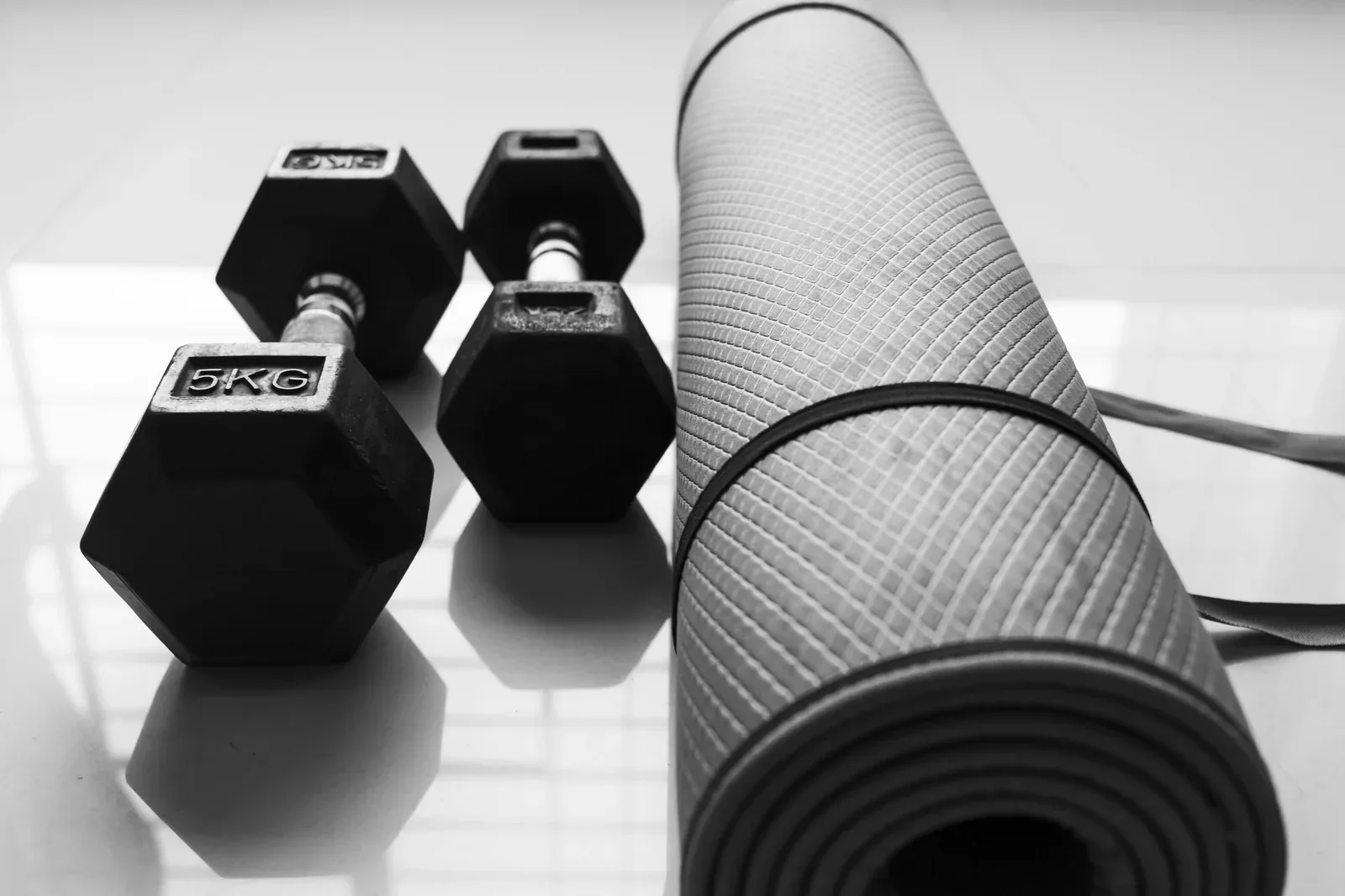 Two 5kg hex dumbbells beside a rolled exercise mat on a tiled floor.