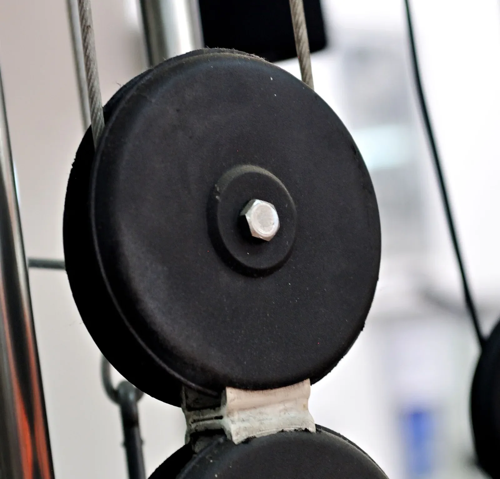 Close-up of a cable-machine pulley, its centre bolt, cable and mounting bracket.