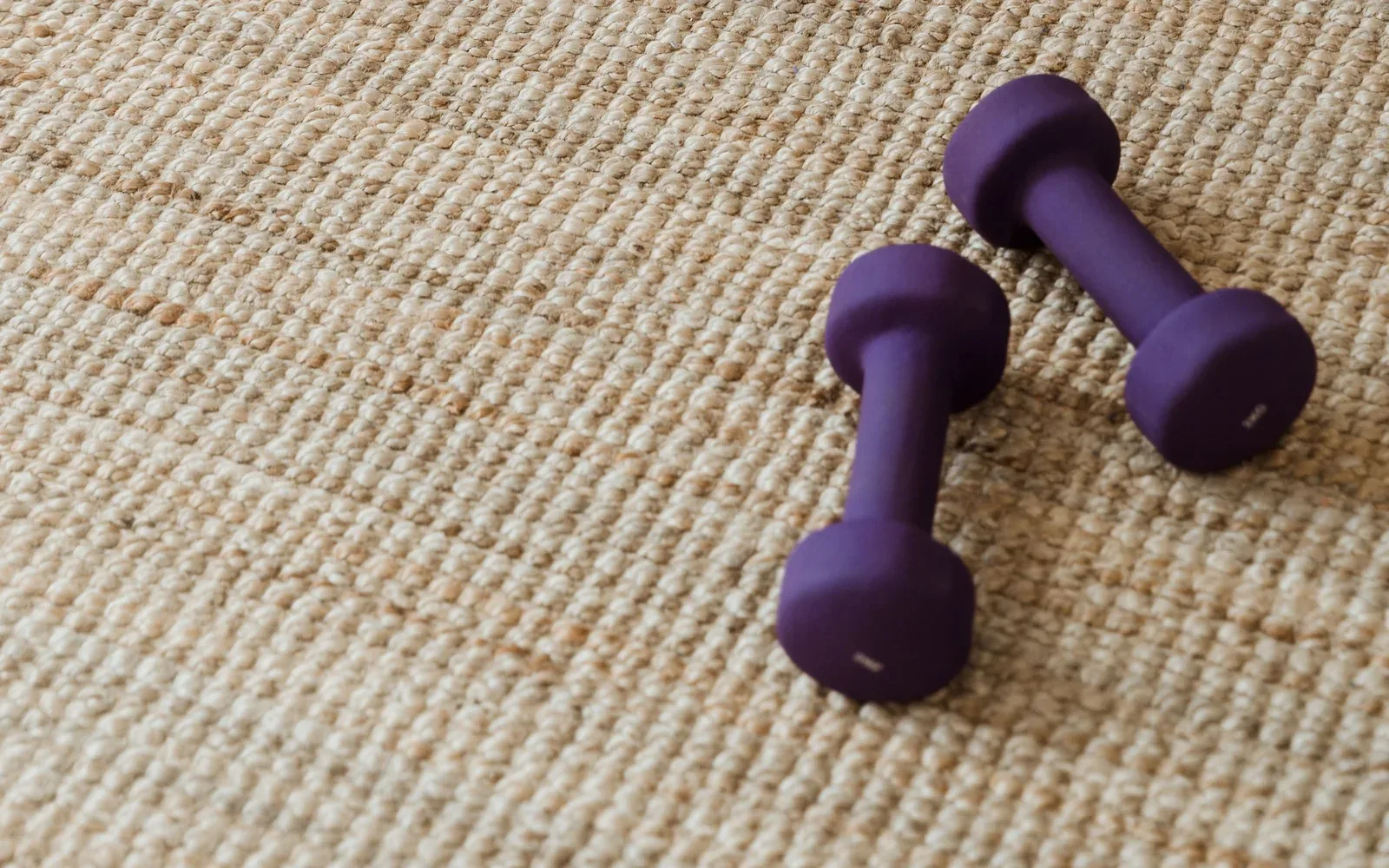 A pair of purple coated dumbbells resting on a woven rug.