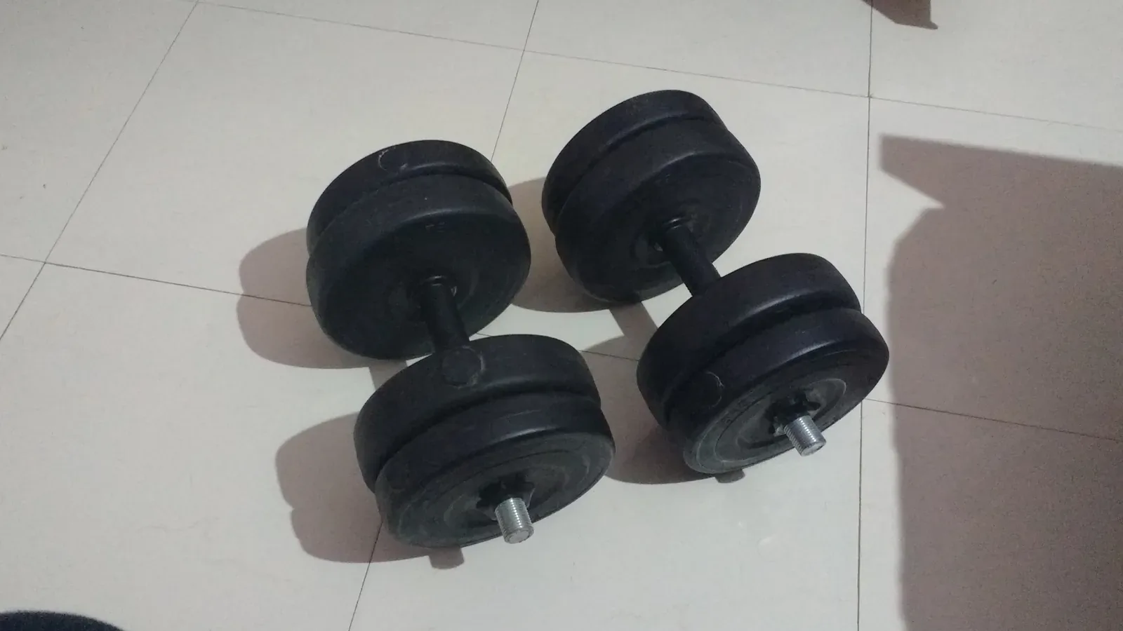 Two plate-loaded dumbbells with removable circular weight discs on a tiled floor.