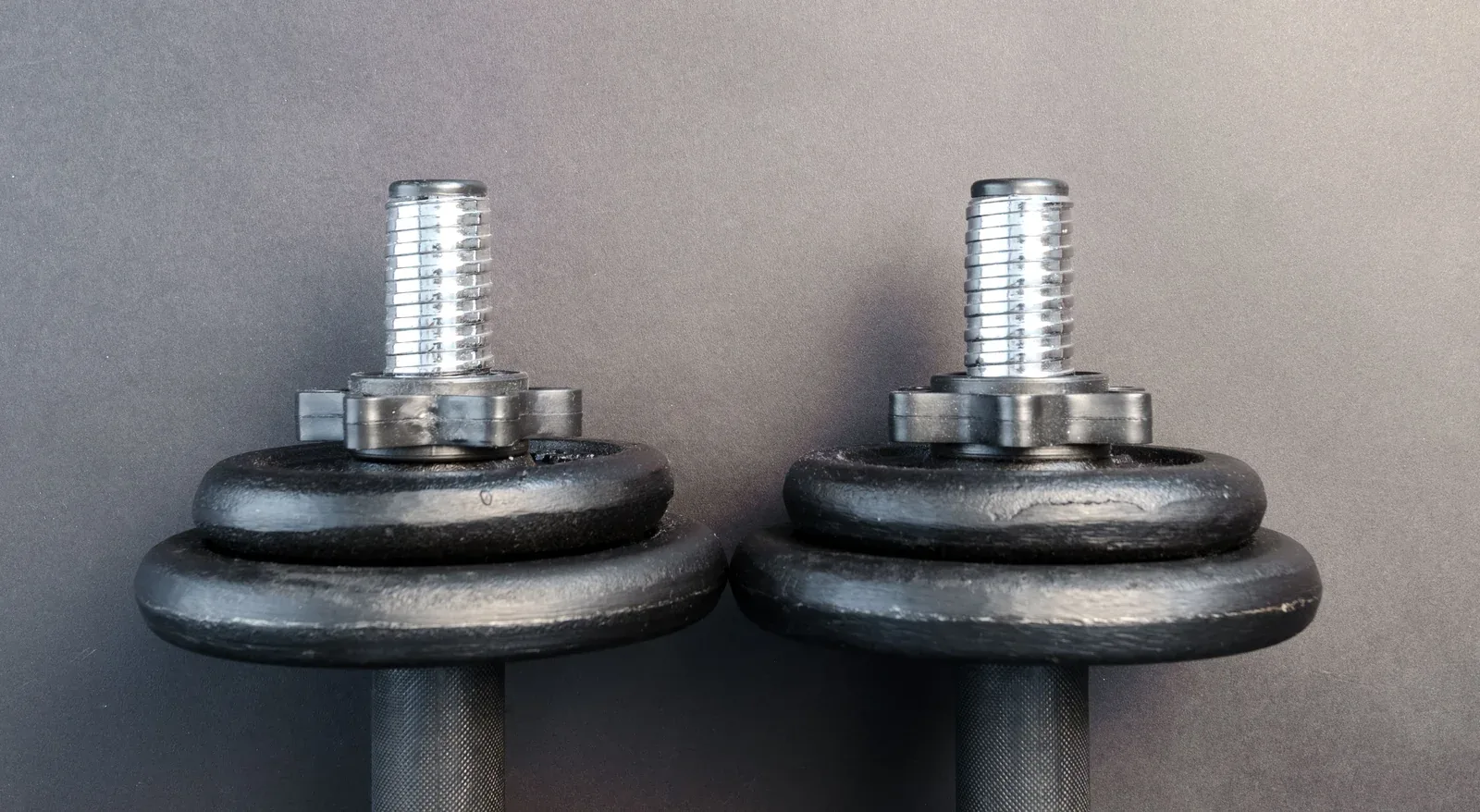Two iron dumbbells with threaded ends and star-shaped collars against a grey background.