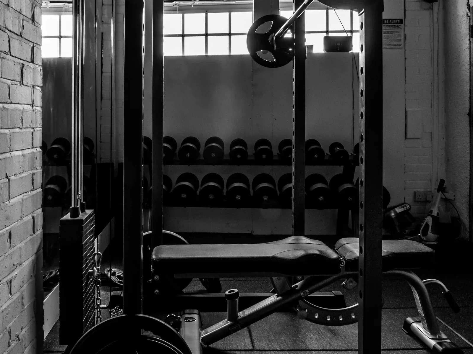 A bench inside a home-gym rack, with a cable stack beside it and dumbbell storage behind.